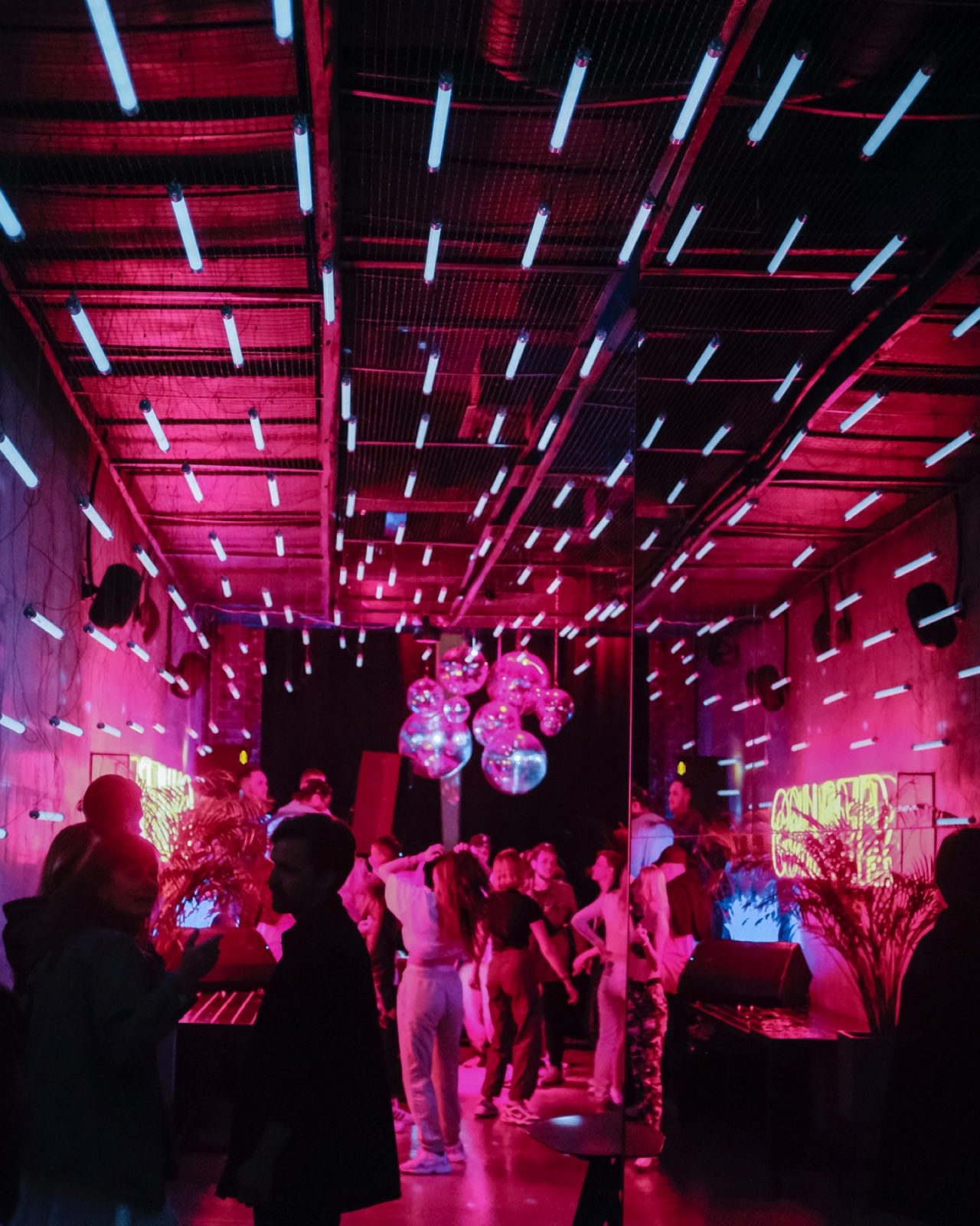 People dancing at a night club with disco balls and pink neon lights