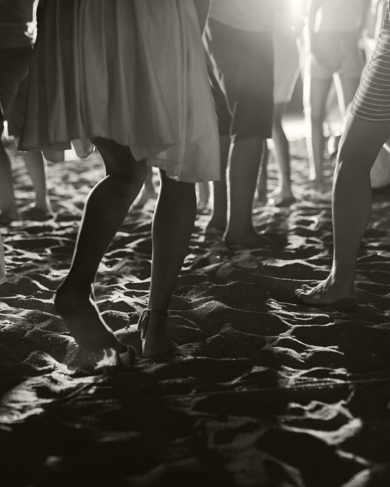 Black and white closeup of people's legs at a nighttime beach dance party
