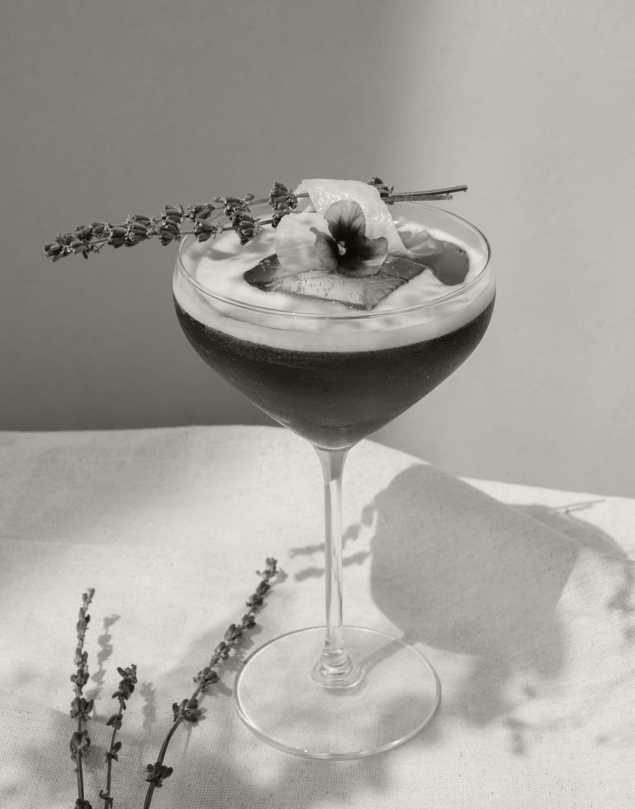 Black and white closeup of a cocktail in a coup glass with flower garnish