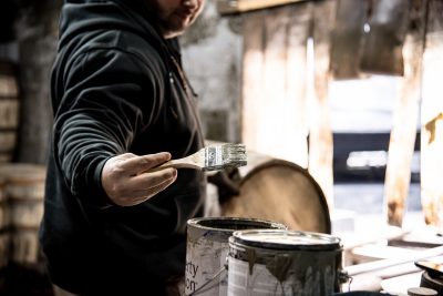 Employee painting oak barrels with two cans of paint