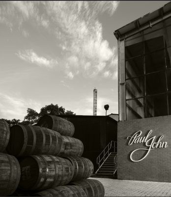 Black and white view outside Paul john Distillery with stack of barrels