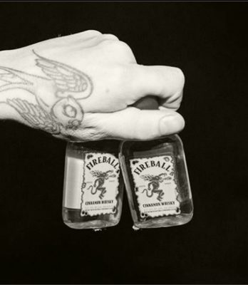 Black and white closeup of hand holding two mini Fireball bottles