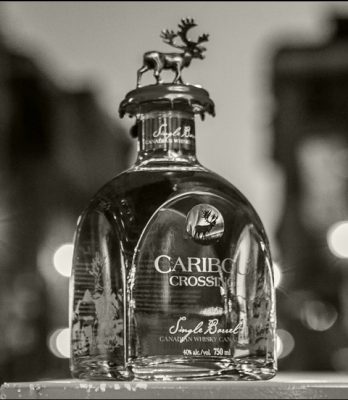 Black and white close up of Caribou Crossing bottle with blurred buildings in the background