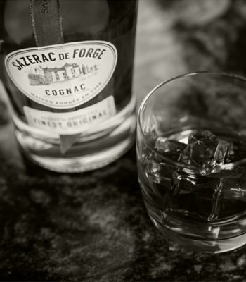 Black and white closeup of Sazerac de Forge Cognac bottle and old fashioned in rocks glass