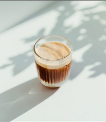 Coffee in glass on white table with tree shadows