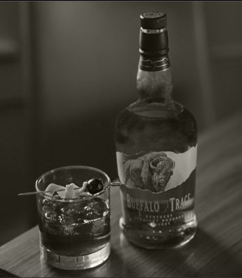 Black and white image of Buffalo Trace Bourbon cocktail and bottle on table
