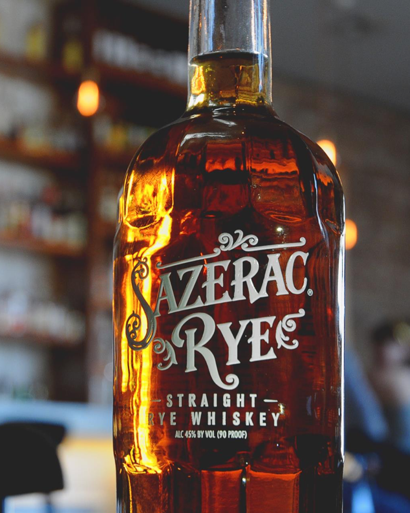 A close up image of a 1 liter bottle of Sazerac Rye - Straight Rye Whiskey with a bar in the background