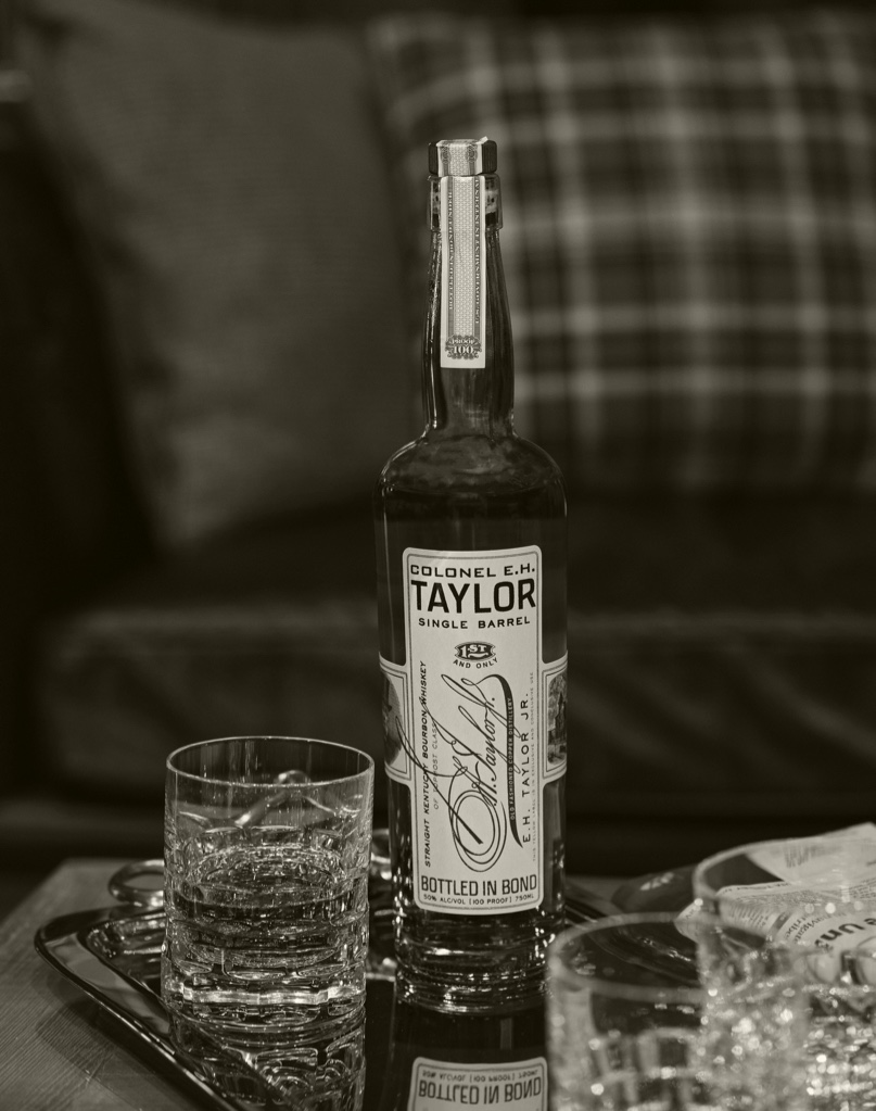 A whiskey glass with a unopened bottle of Colonel E.H. Taylor Single Barrel Straight Kentucky Bourbon Whiskey