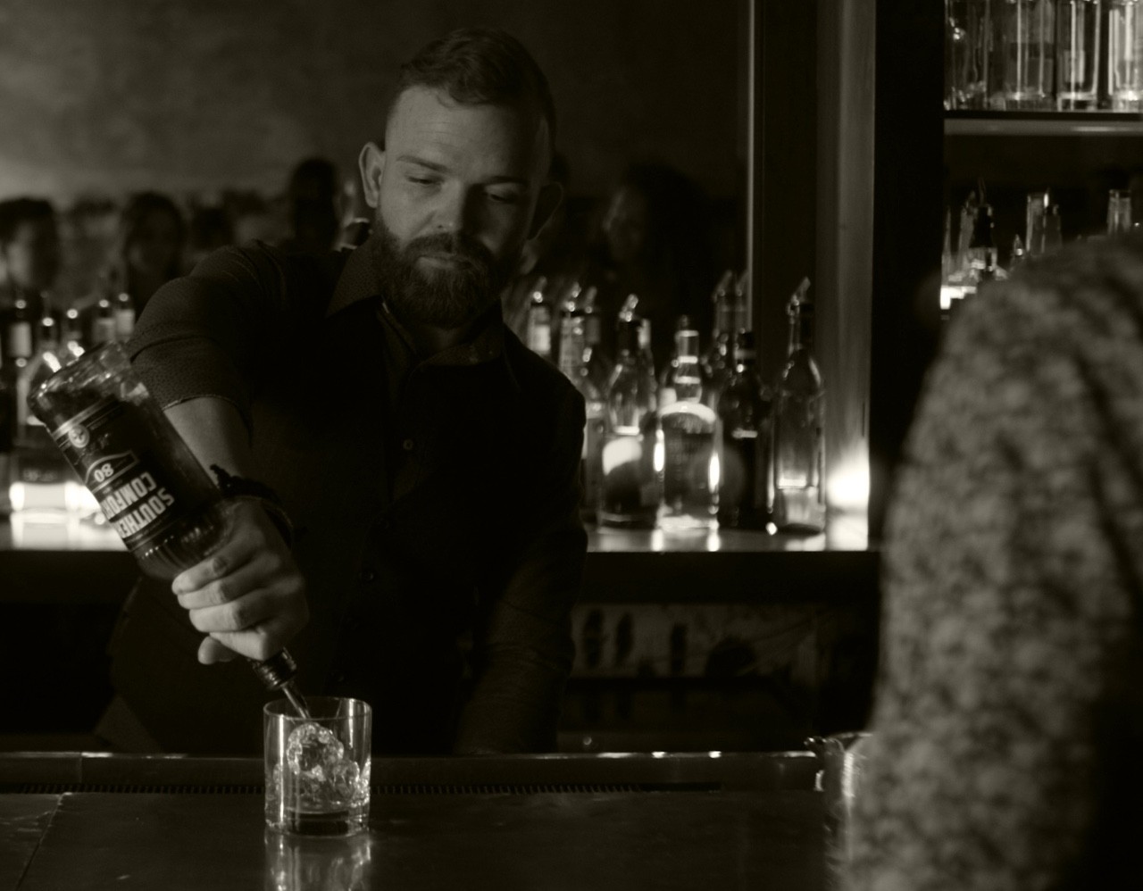 A male bartender pouring a glass of Southern Comfort for a customer