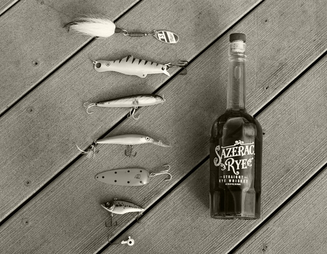 A bottle of Sazerac Rye lying next to fishing lures on a dock 