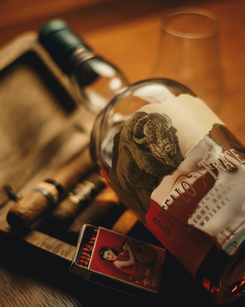 A half empty bottle of Buffalo Trace Kentucky Straight Bourbon Whiskey with cigars and a pack of matches with a woman on the case