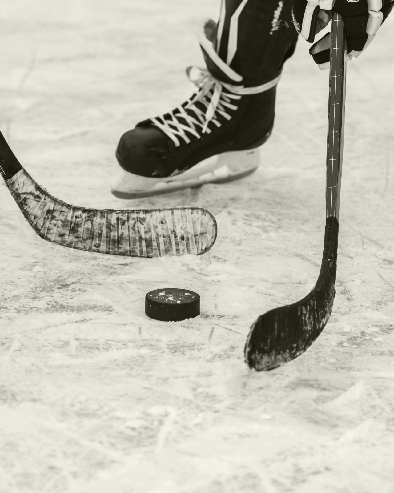 Black and white closeup of two hockey sticks going after hockey puck