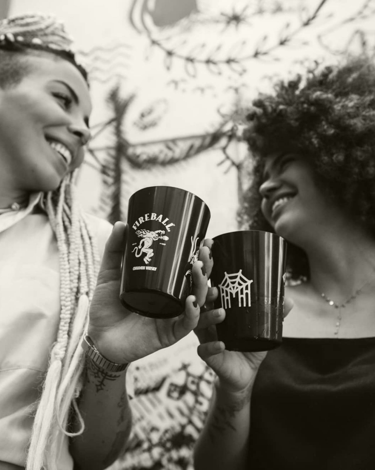 Black and white image of two women smiling and cheersing Fireball cups